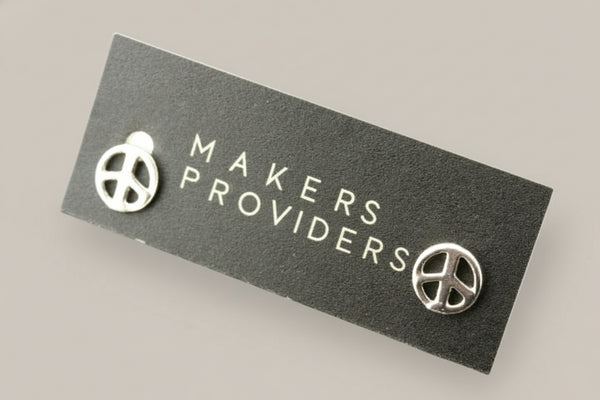 Silver peace sign earrings on a 'Makers & Provide' card against a gray background