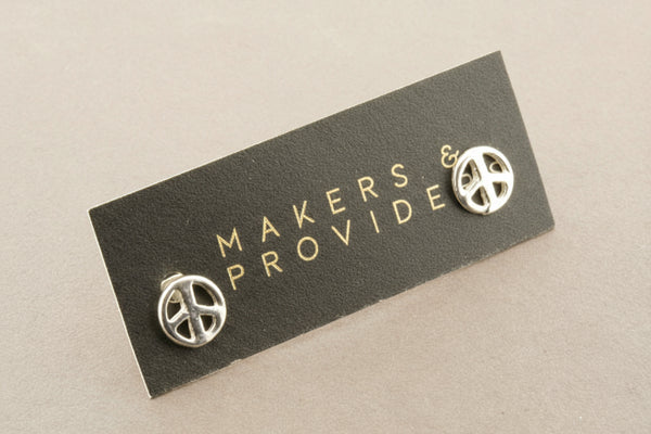 Silver peace symbol earrings on a 'Makers & Provide' card against a gray background