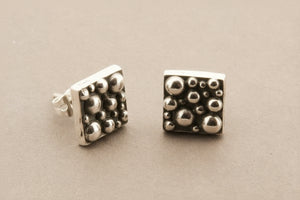 Pair of silver square stud earrings with textured design on a gray background