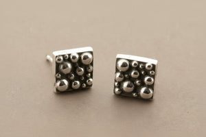 Pair of silver square stud earrings with textured design on a gray background