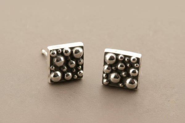 Pair of silver square stud earrings with textured design on a gray background