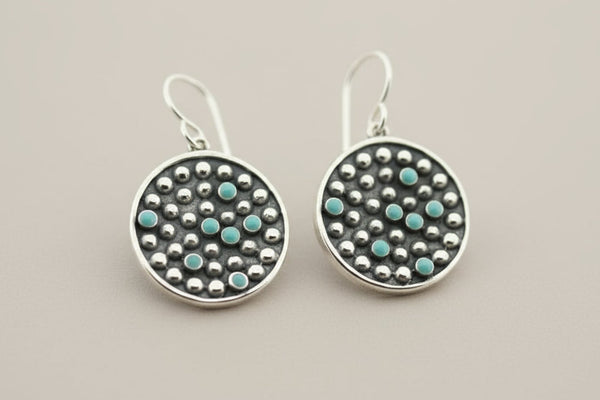 Pair of silver earrings with turquoise stones on a gray background