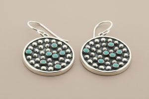 Pair of silver earrings with turquoise stones on a gray background