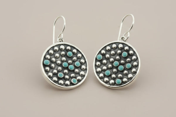 Pair of silver earrings with turquoise stones on a gray background