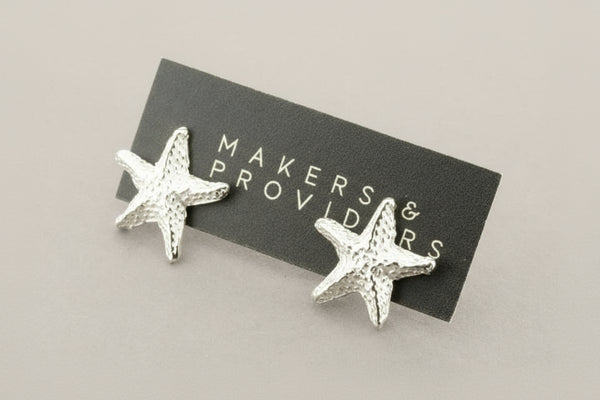 Silver starfish earrings on a 'Makers & Providers' card against a gray background