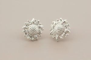 Silver sunflower-shaped earrings on a gray background