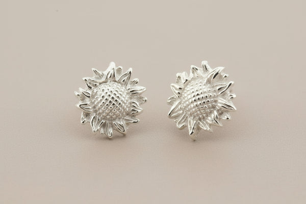 Silver sunflower-shaped earrings on a gray background