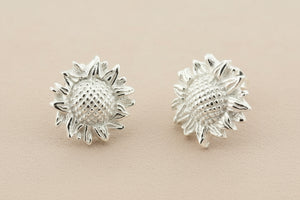 Pair of silver sunflower-shaped earrings on a gray background