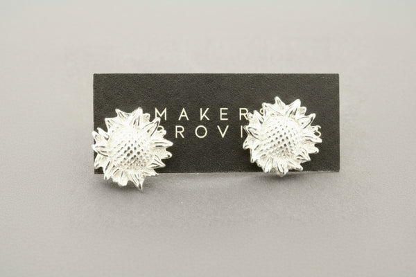 Silver sunflower-shaped earrings, against a gray background.