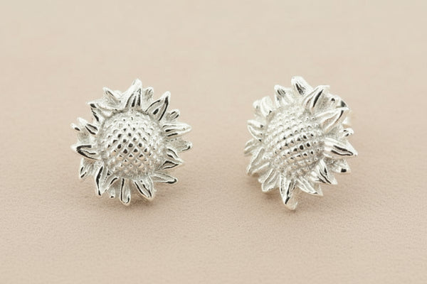 Pair of silver sunflower-shaped earrings on a gray background