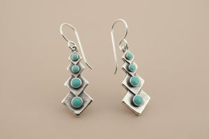 Pair of silver earrings with turquoise stones on a gray background