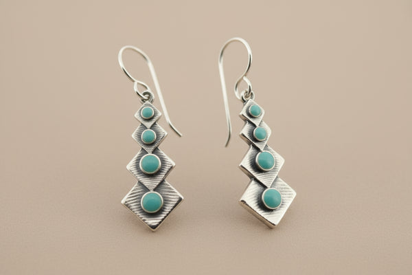 Pair of silver earrings with turquoise stones on a gray background