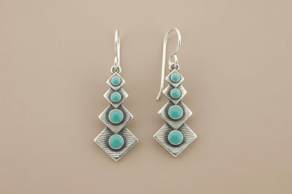 Pair of silver earrings with turquoise stones on a gray background