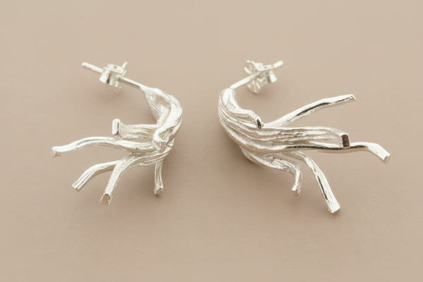 Silver branch-like earrings on a dark gray background