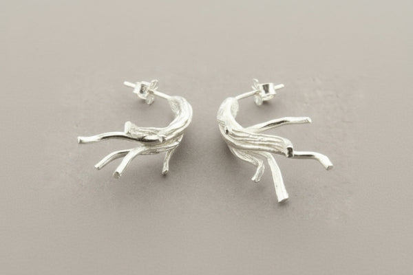 Silver branch-like earrings on a dark gray background