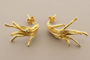 Gold branch-like earrings on a gray background