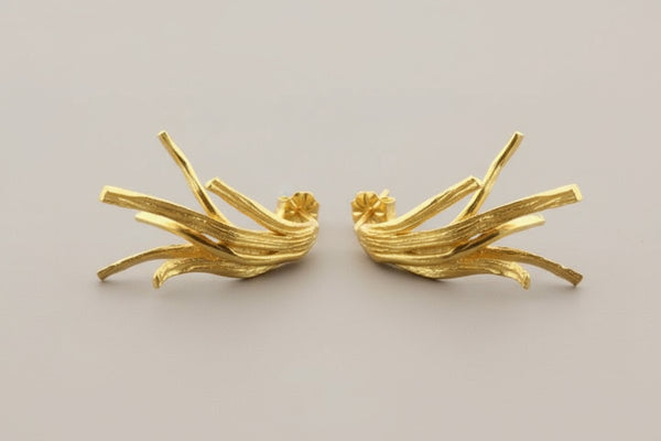 Pair of gold branch-shaped earrings on a gray background