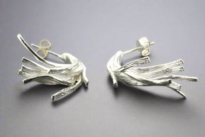 Pair of silver leaf-like earrings on a gray background