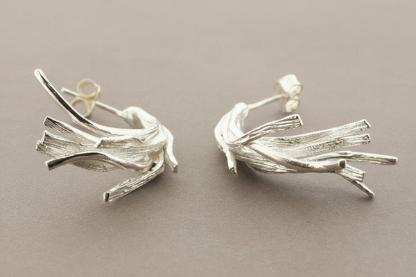 Pair of silver leaf-like earrings on a gray background