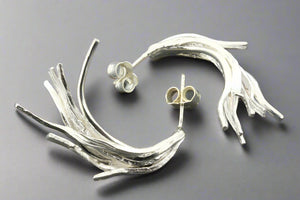 Silver twig-like earrings on a dark gray background