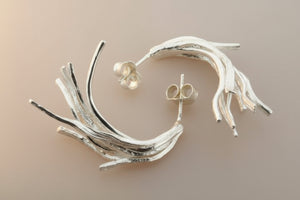 Silver twig-like earrings on a dark gray background