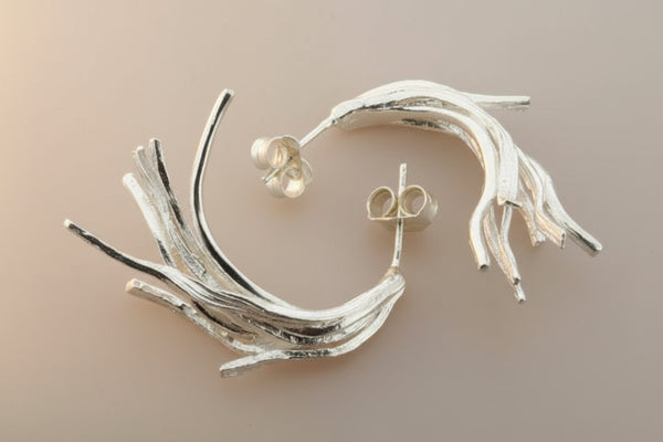 Silver twig-like earrings on a dark gray background