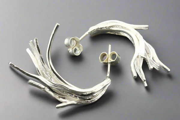 Silver twig-like earrings on a dark gray background
