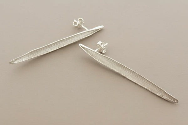 Pair of silver leaf-shaped earrings on a gray background