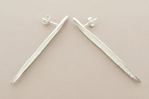 Pair of silver leaf-shaped earrings on a gray background