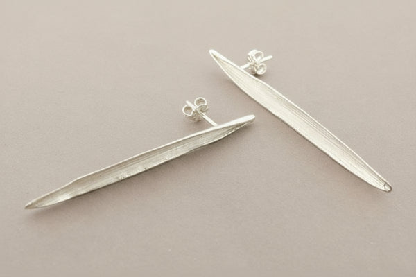 Pair of silver leaf-shaped earrings on a gray background
