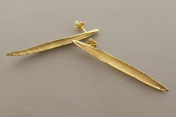 Gold leaf-shaped earrings on a gray background