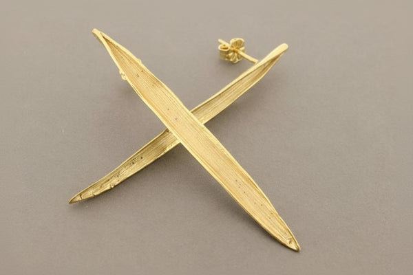 Gold earrings shaped like stylized crosses on a gray background