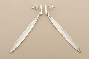 Pair of silver leaf-shaped earrings on a gray background