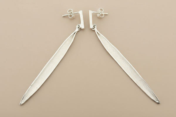 Pair of silver leaf-shaped earrings on a gray background
