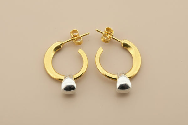 Gold hoop earrings with silver teardrop pendants on a gray background