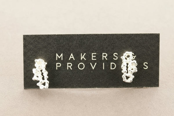 Pair of silver earrings on a 'MAKERS PROVIDES' card against a light gray background