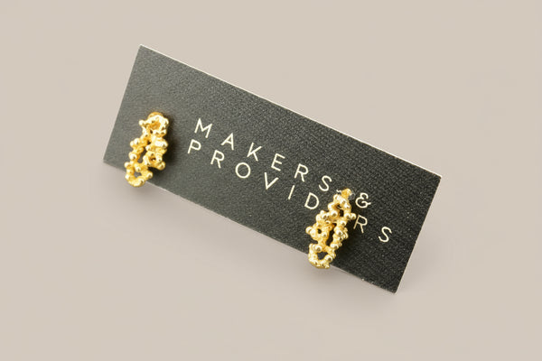 Gold earrings on a 'Makers & Providers' card against a gray background