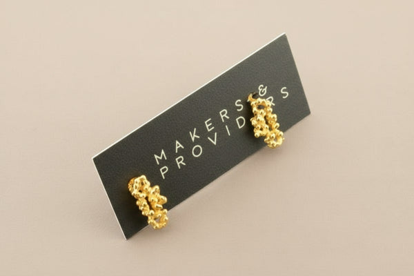 Gold earrings on a 'Makers & Providers' card against a gray background