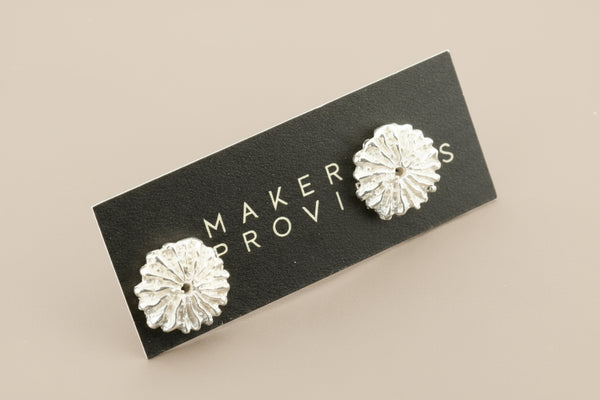 Silver floral earrings on a 'Maker Provisions' card against a gray background