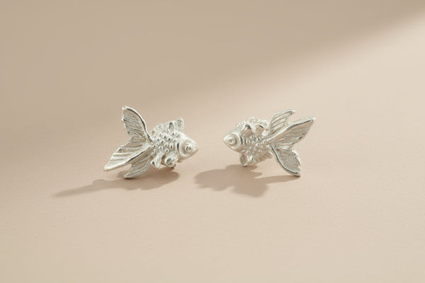 Silver fish-shaped earrings on a gray background