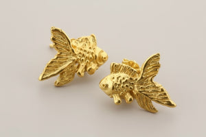 Gold fish-shaped earrings on a gray background