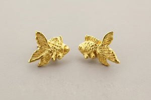 Gold fish-shaped earrings on a gray background
