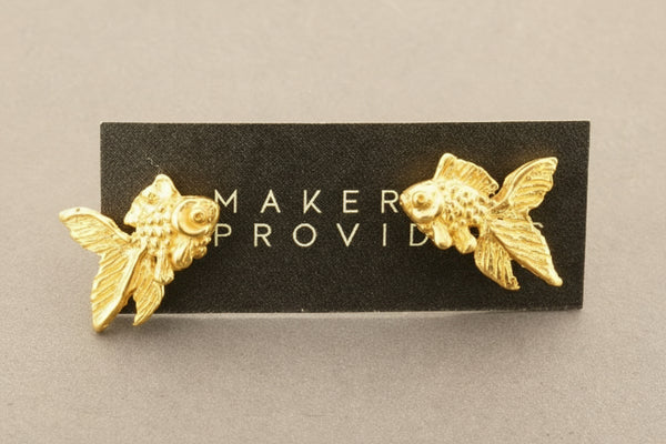 Gold fish-shaped earrings on a black card with 'Maker Provid' branding.