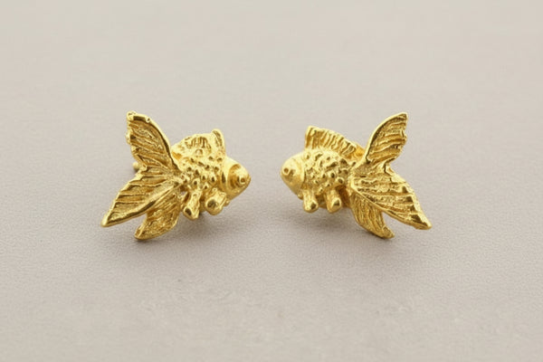 Gold fish-shaped earrings on a gray background