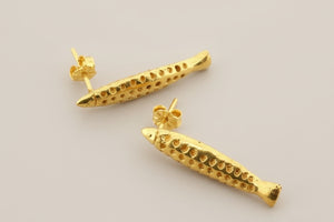 Gold fish-shaped earrings on a gray background