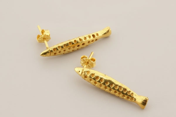 Gold fish-shaped earrings on a gray background