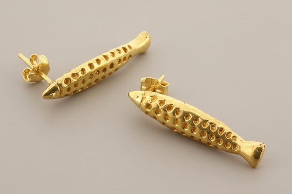 Gold fish-shaped earrings on a gray background