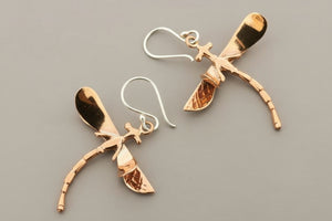 Pair of copper dragonfly earrings on a gray background