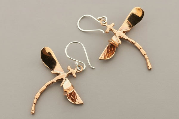 Pair of copper dragonfly earrings on a gray background