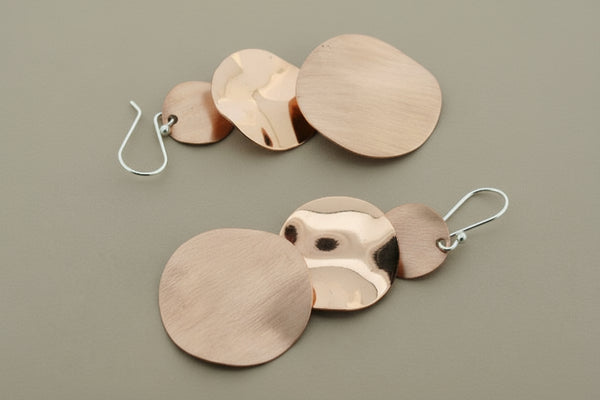 Pair of copper disc earrings on a dark gray background